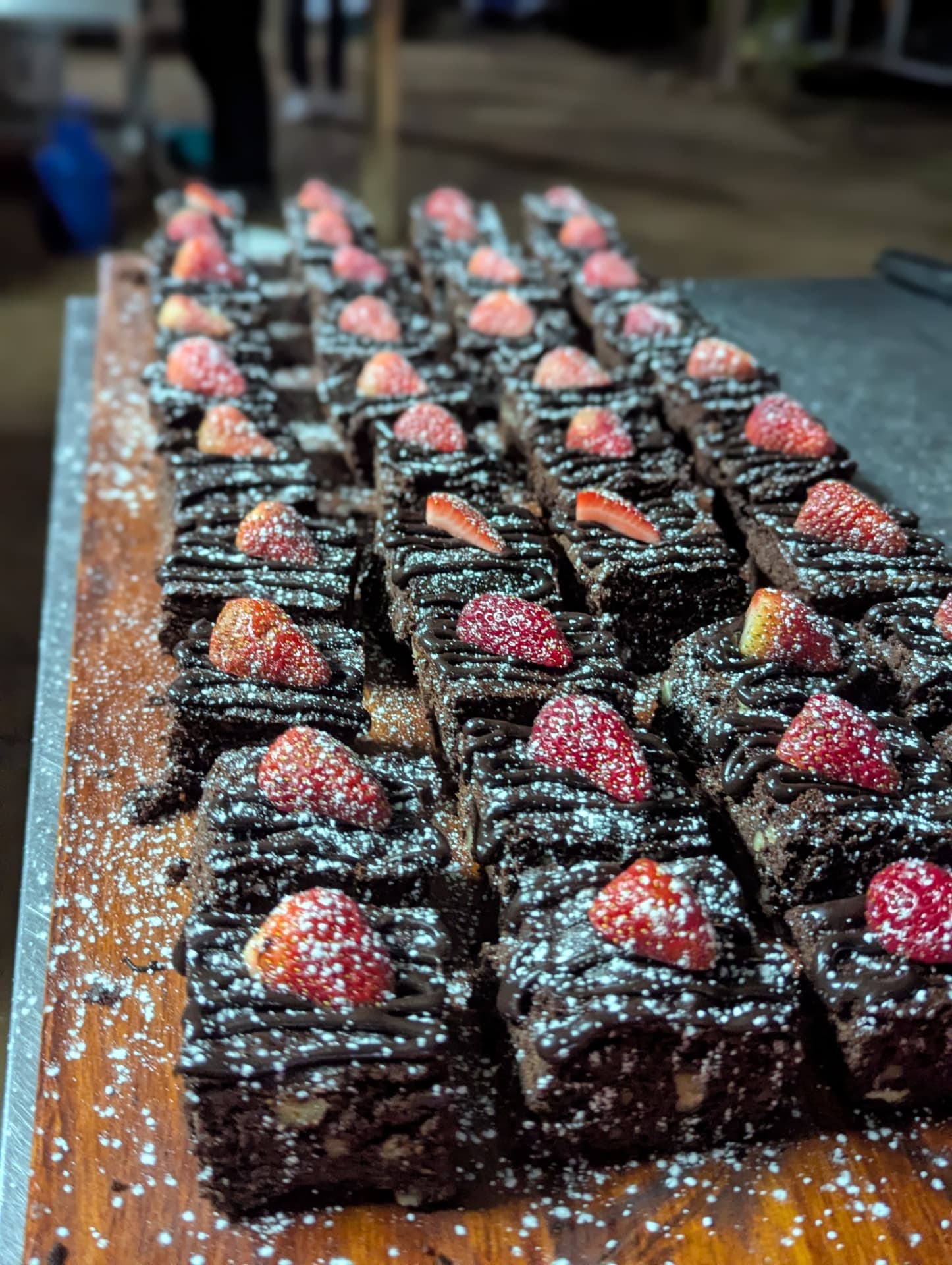 Chocolate brownies with strawberries and icing sugar on a wooden board